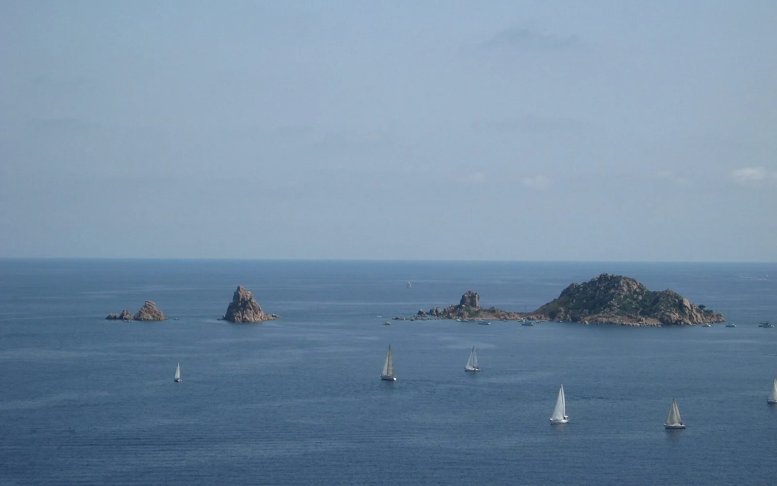 Barche a vela in regata sul mare della Sardegna, davanti a isolotti di granito